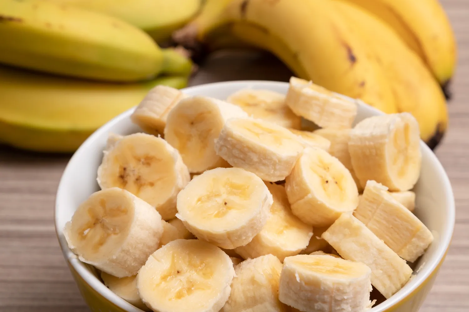 Sliced bananas in a bowl with whole bananas in the background