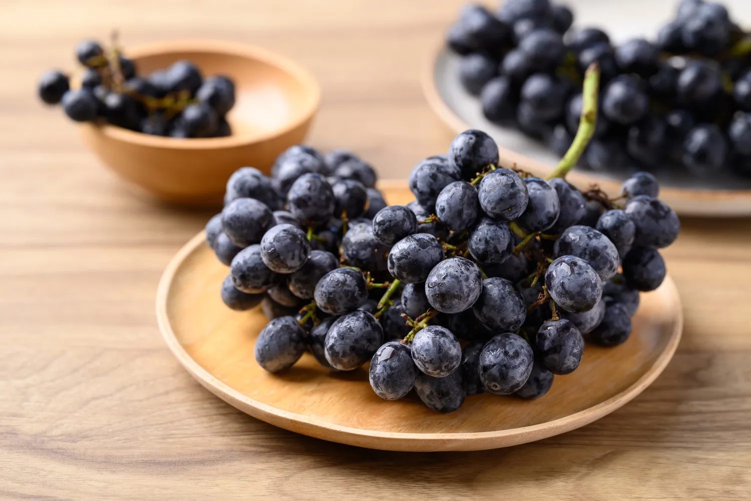 Bunches of grapes arranged on wooden plates and bowls on a table