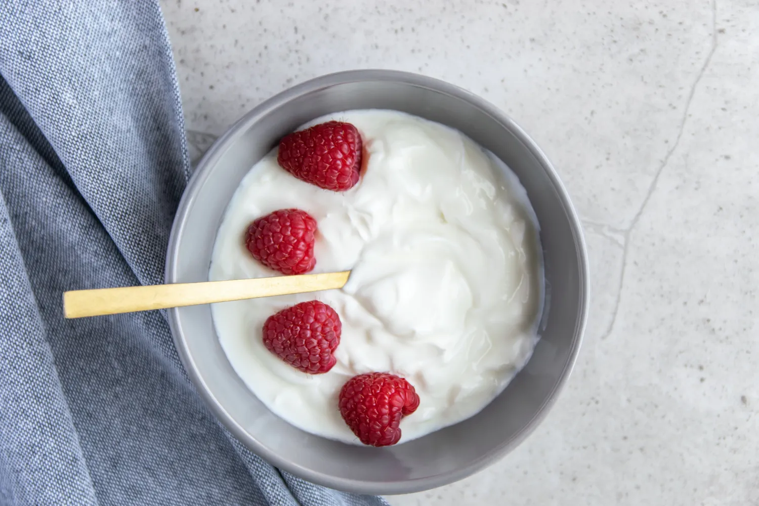 A bowl of yogurt with raspberries and a wooden spoon
